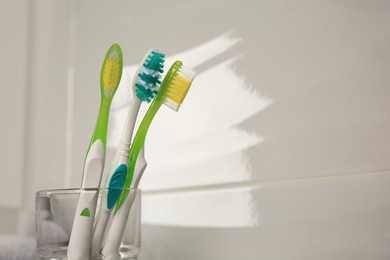 Photo of Light blue and green toothbrushes near white wall, space for text