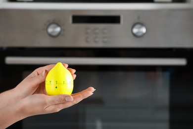 Woman holding kitchen timer in shape of lemon near oven, closeup. Space for text
