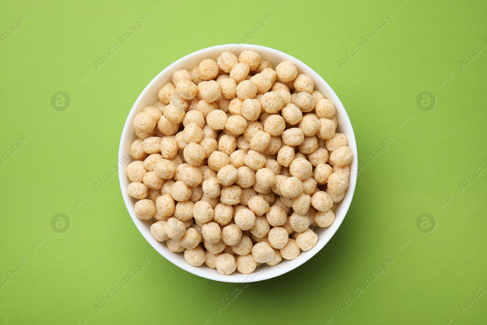 Photo of Tasty cereal balls in bowl on green table, top view