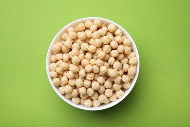 Tasty cereal balls in bowl on green table, top view