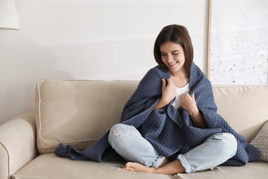 Photo of Woman covered with warm dark blue plaid sitting on sofa at home