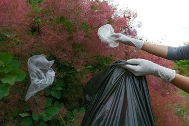 Photo of Woman with trash bag collecting garbage in park, closeup