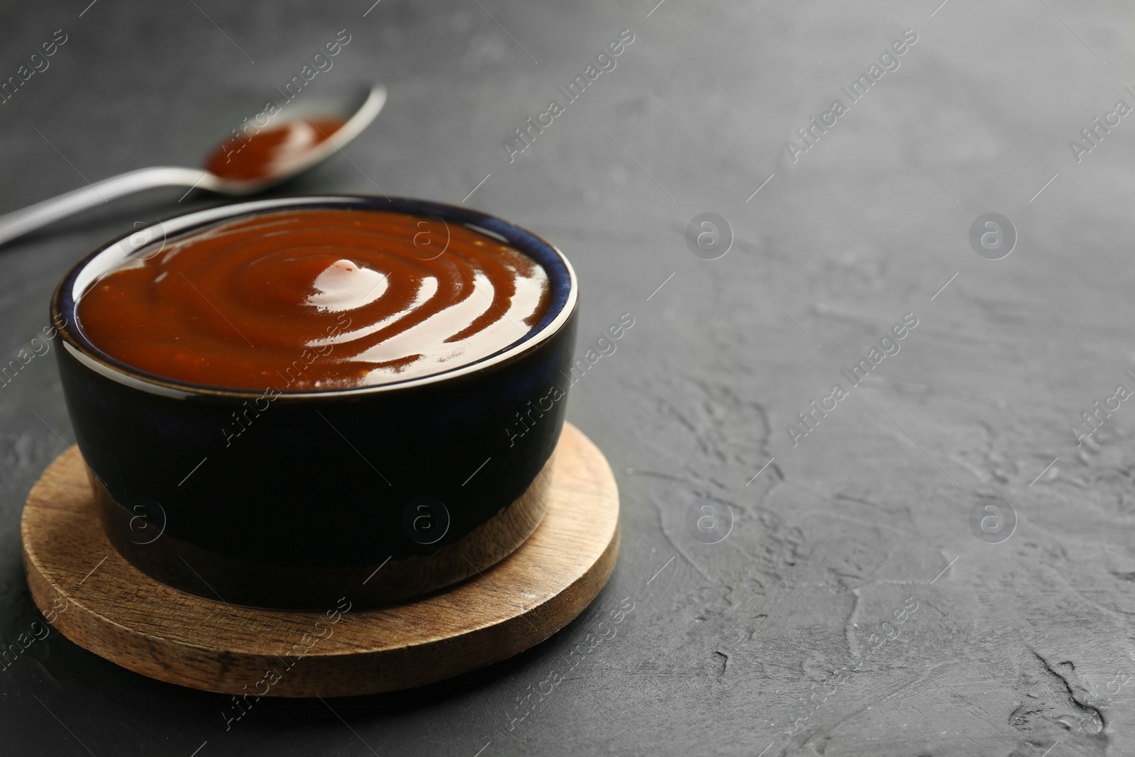 Photo of Tasty barbeque sauce in bowl on dark textured table, closeup. Space for text