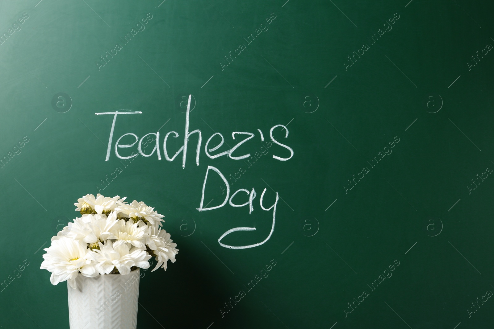 Photo of Vase of flowers near green chalkboard with inscription TEACHER'S DAY. Space for text