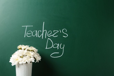 Vase of flowers near green chalkboard with inscription TEACHER'S DAY. Space for text