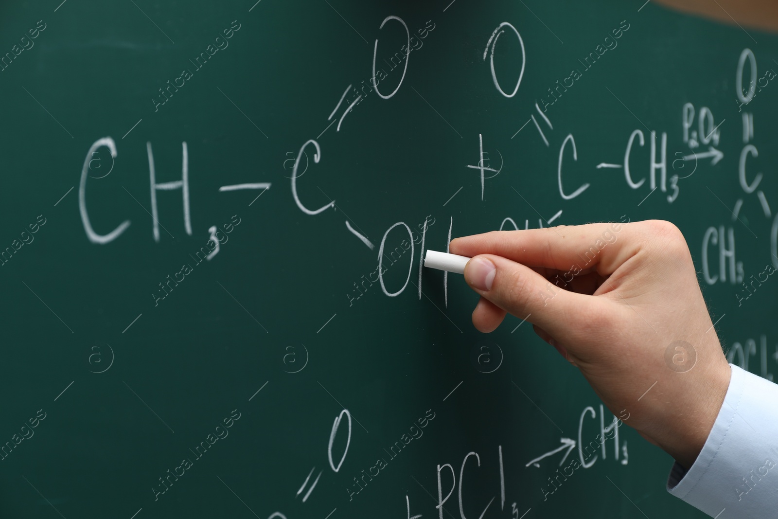 Photo of Teacher writing chemical formulas with chalk on green chalkboard, closeup