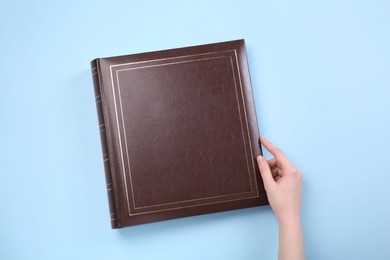 Photo of Woman with photo album at light blue background, top view