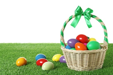 Photo of Wicker basket with Easter eggs on green grass against white background. Space for text
