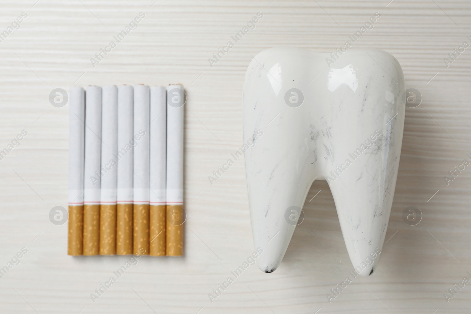 Photo of Damaged tooth model and cigarettes on white wooden table, flat lay