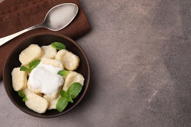 Photo of Bowl of tasty lazy dumplings with sour cream and mint leaves on brown table, flat lay. Space for text