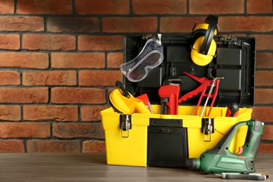 Photo of Box with different tools for repair on wooden table near brick wall, space for text