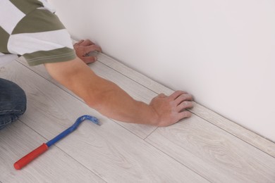 Photo of Professional worker using nail puller during installationnew laminate flooring indoors, closeup