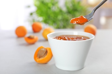 Photo of Bowl and spoon with tasty apricot jam on table