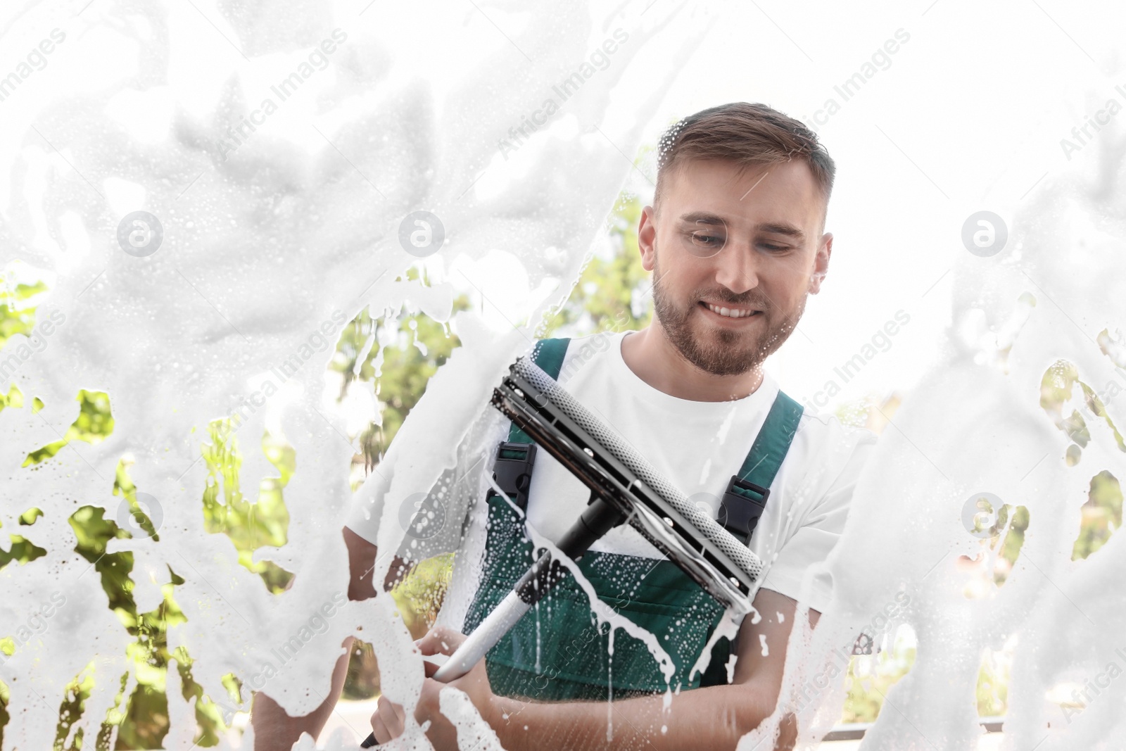 Photo of Male cleaner wiping window glass with squeegee from outside