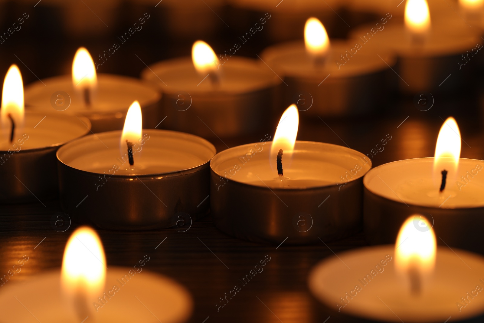 Photo of Burning tealight candles on dark surface, closeup