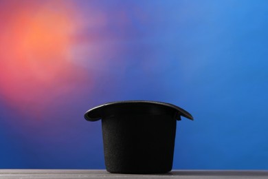 Magician's hat on wooden table against color background, space for text