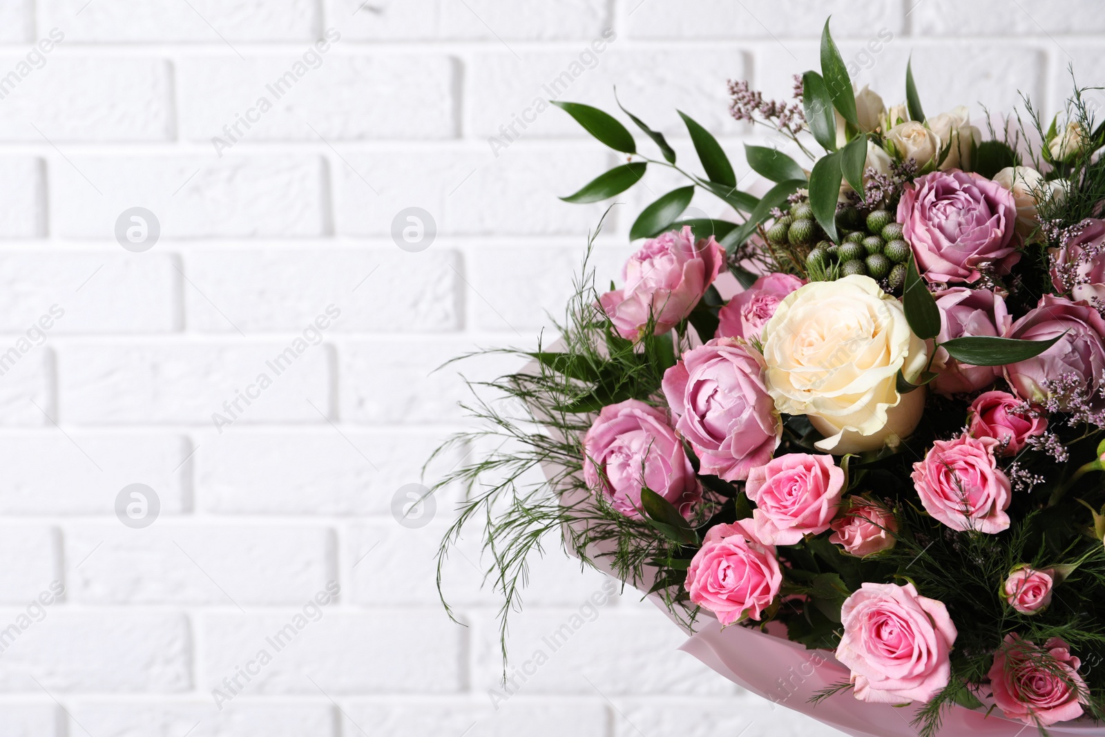 Photo of Beautiful bouquet with roses near white brick wall. Space for text