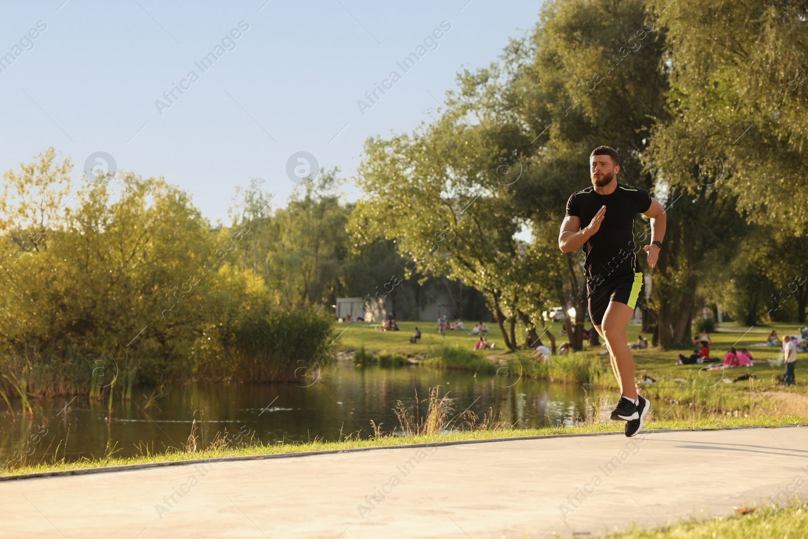 Photo of Young man running near pond in park. Space for text