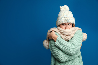 Image of Young woman wearing hat and scarf suffering from fever on blue background, space for text. Cold symptoms