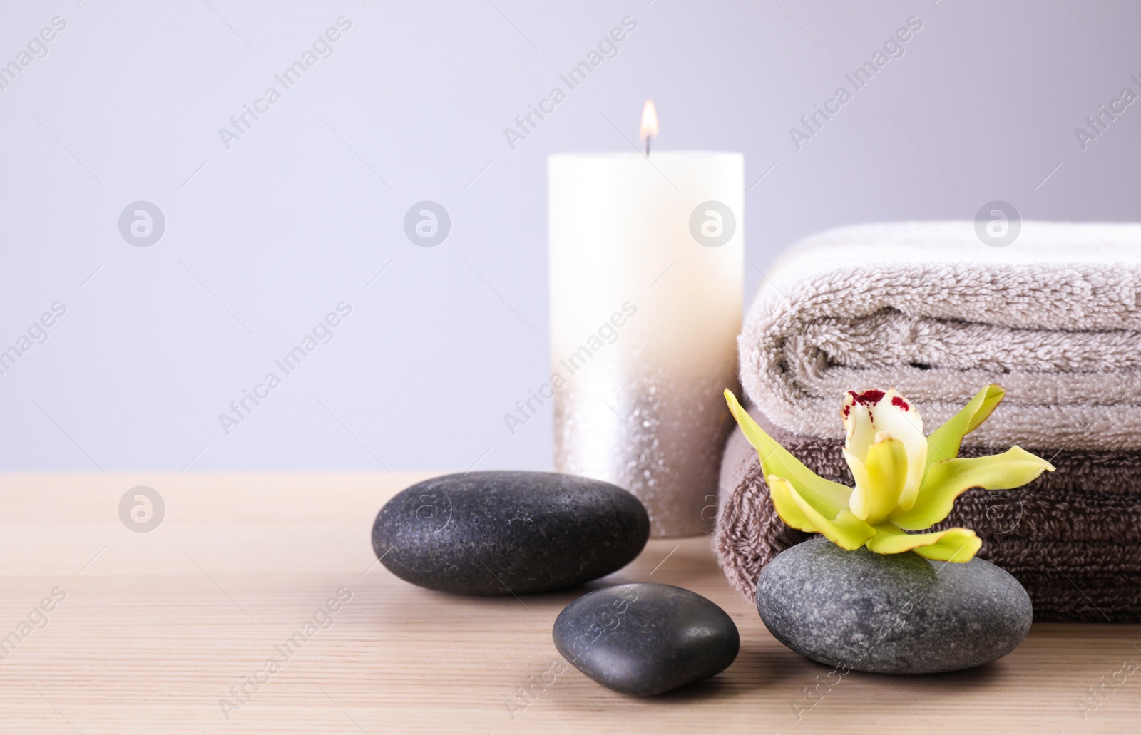 Photo of Spa stones with exotic flower, burning candle and fresh towels on wooden table, space for text