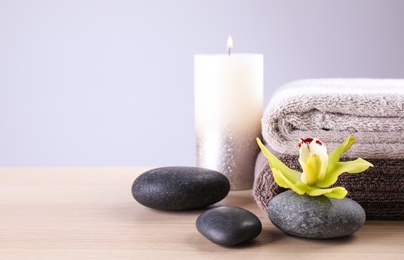 Photo of Spa stones with exotic flower, burning candle and fresh towels on wooden table, space for text