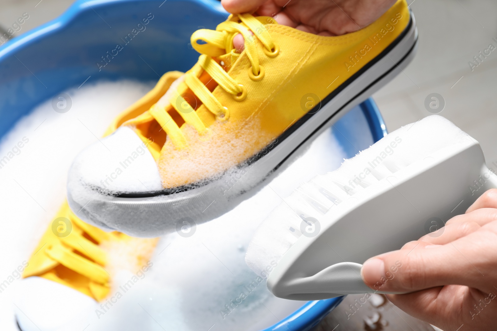 Photo of Woman cleaning stylish sneakers with brush in wash basin, closeup