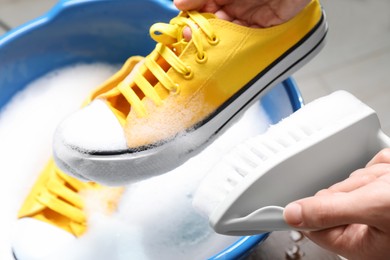Photo of Woman cleaning stylish sneakers with brush in wash basin, closeup