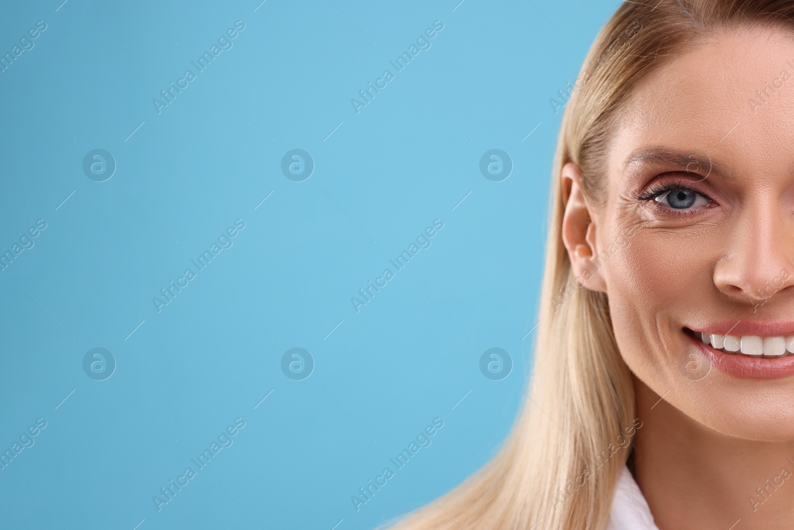 Photo of Portrait of smiling middle aged woman on light blue background, closeup. Space for text