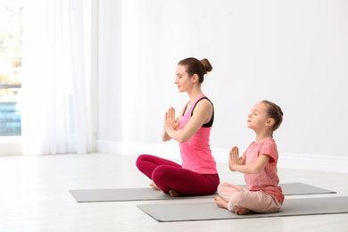 Young mother with little daughter practicing yoga at home