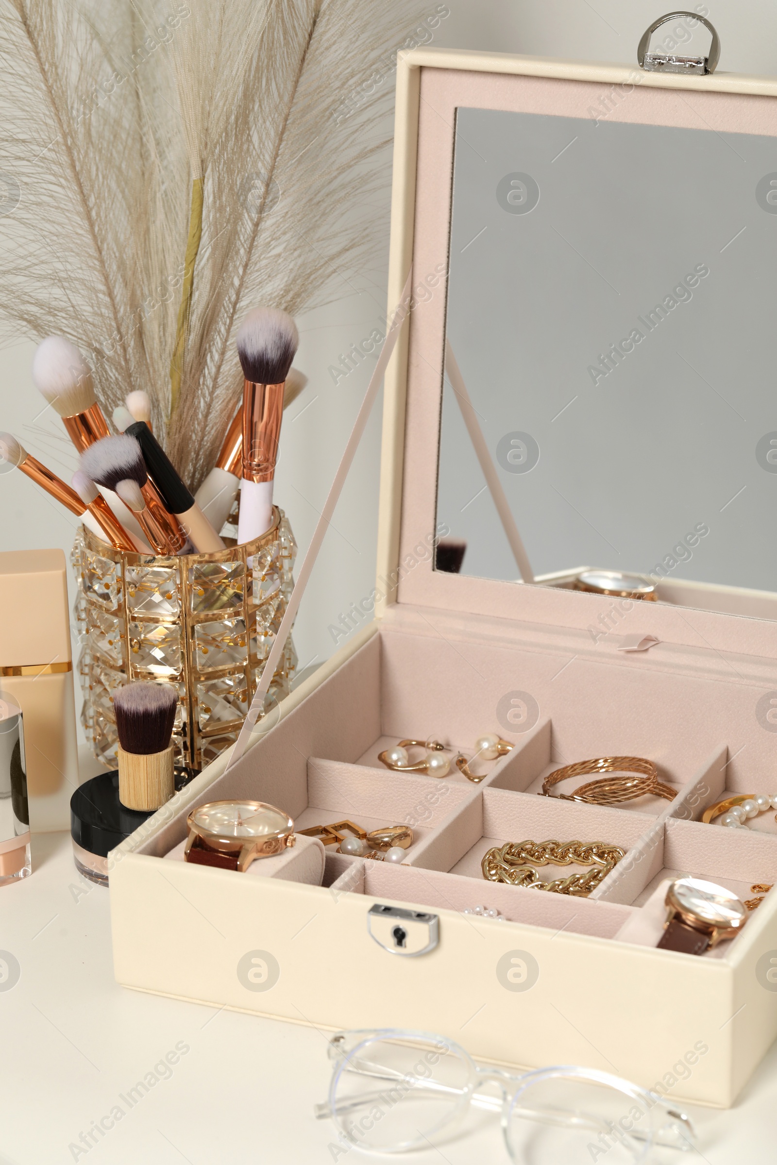 Photo of Jewelry box with many different accessories, makeup brushes and glasses on white table