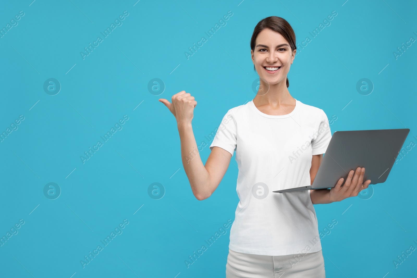 Photo of Special promotion. Happy woman with laptop pointing at something on light blue background, space for text