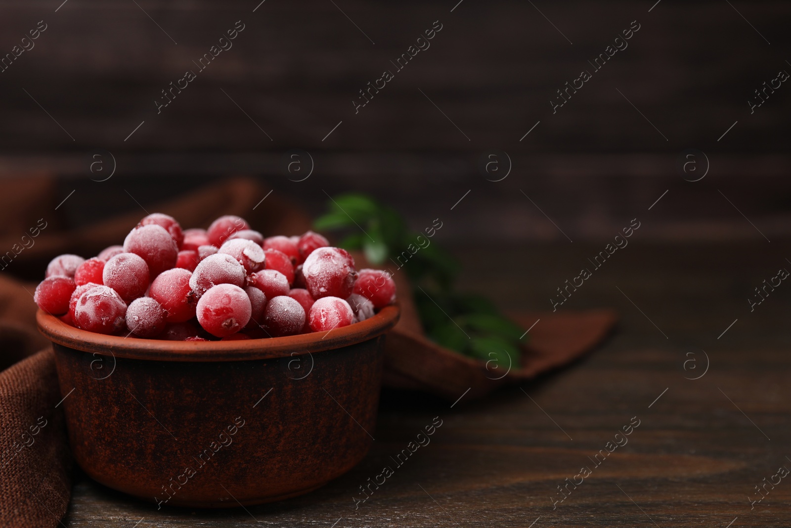 Photo of Frozen red cranberries in bowl on wooden table, closeup. Space for text