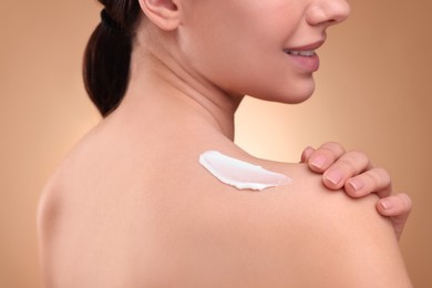 Woman with smear of body cream on her shoulder against light brown background, closeup