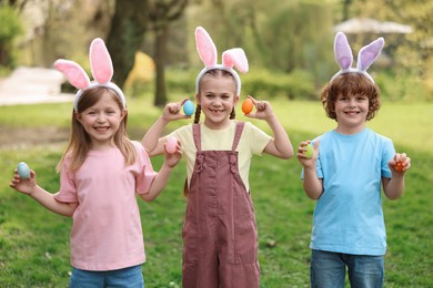 Photo of Easter celebration. Cute little children in bunny ears holding painted eggs outdoors