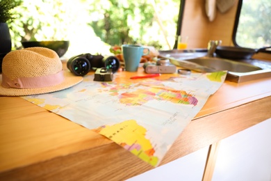 Photo of World map and travel accessories on wooden table in motorhome. Summer trip