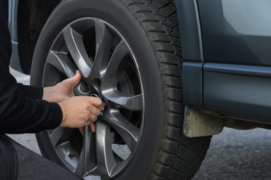 Photo of Man changing tire on car outdoors, closeup