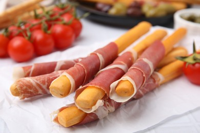 Delicious grissini sticks with prosciutto and snacks on white table, closeup