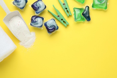 Photo of Different laundry capsules, washing powder and clothespins on yellow background, flat lay. Space for text