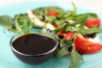 Photo of Bowl of balsamic vinegar on plate with vegetable salad, closeup