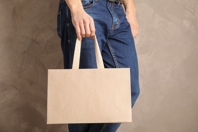 Man holding mock-up of paper shopping bag on color background