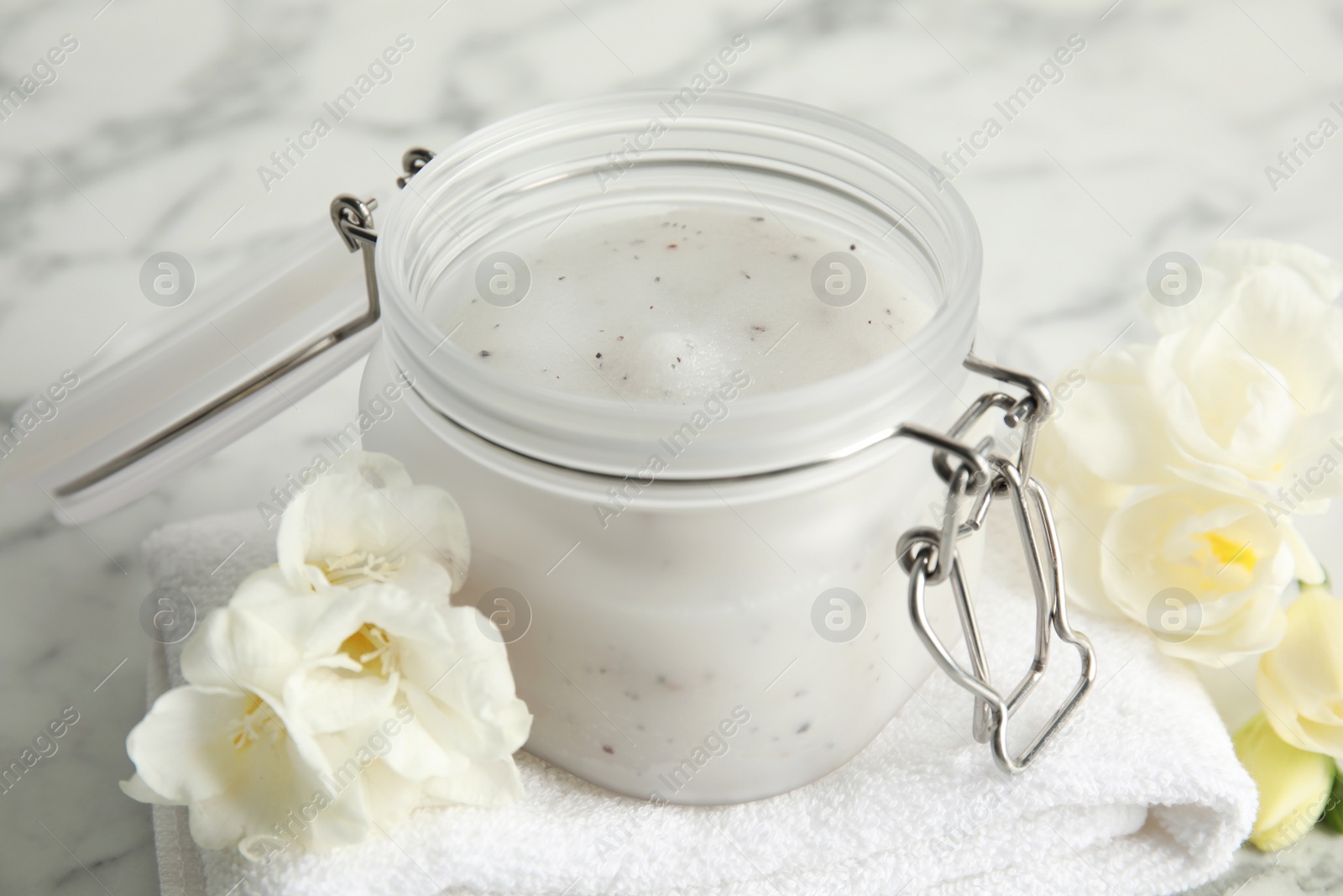 Photo of Jar of salt scrub, freesia flowers and towel on white marble table