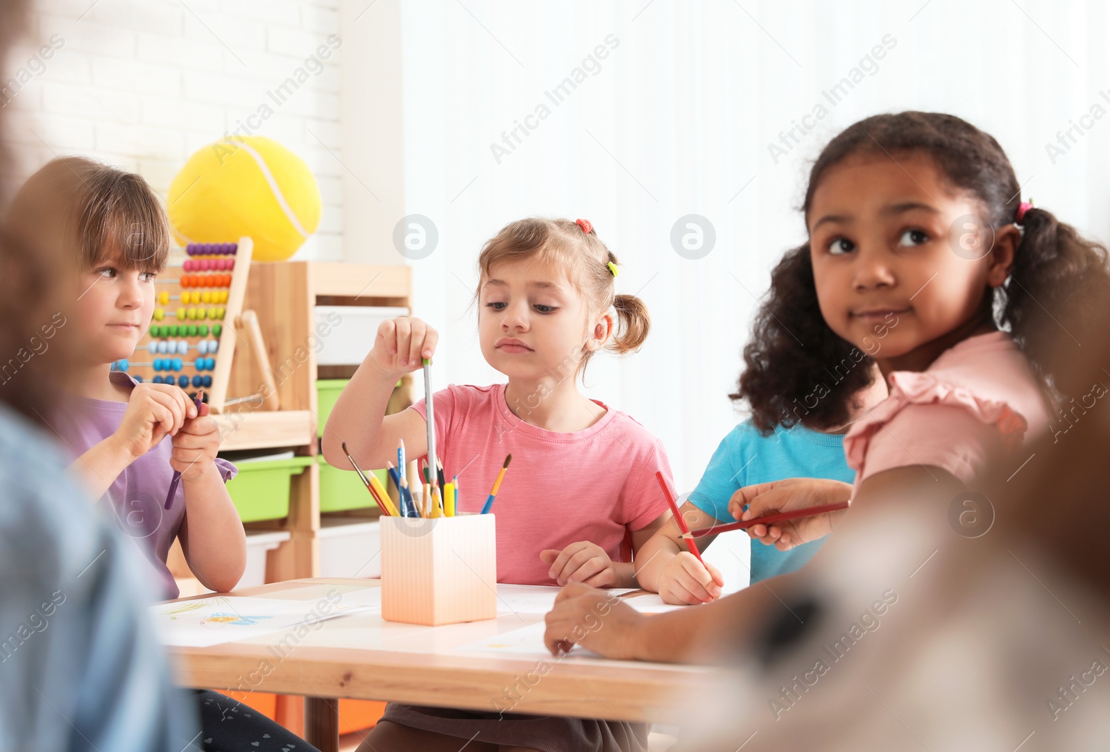 Photo of Adorable children drawing together at table indoors. Kindergarten playtime activities