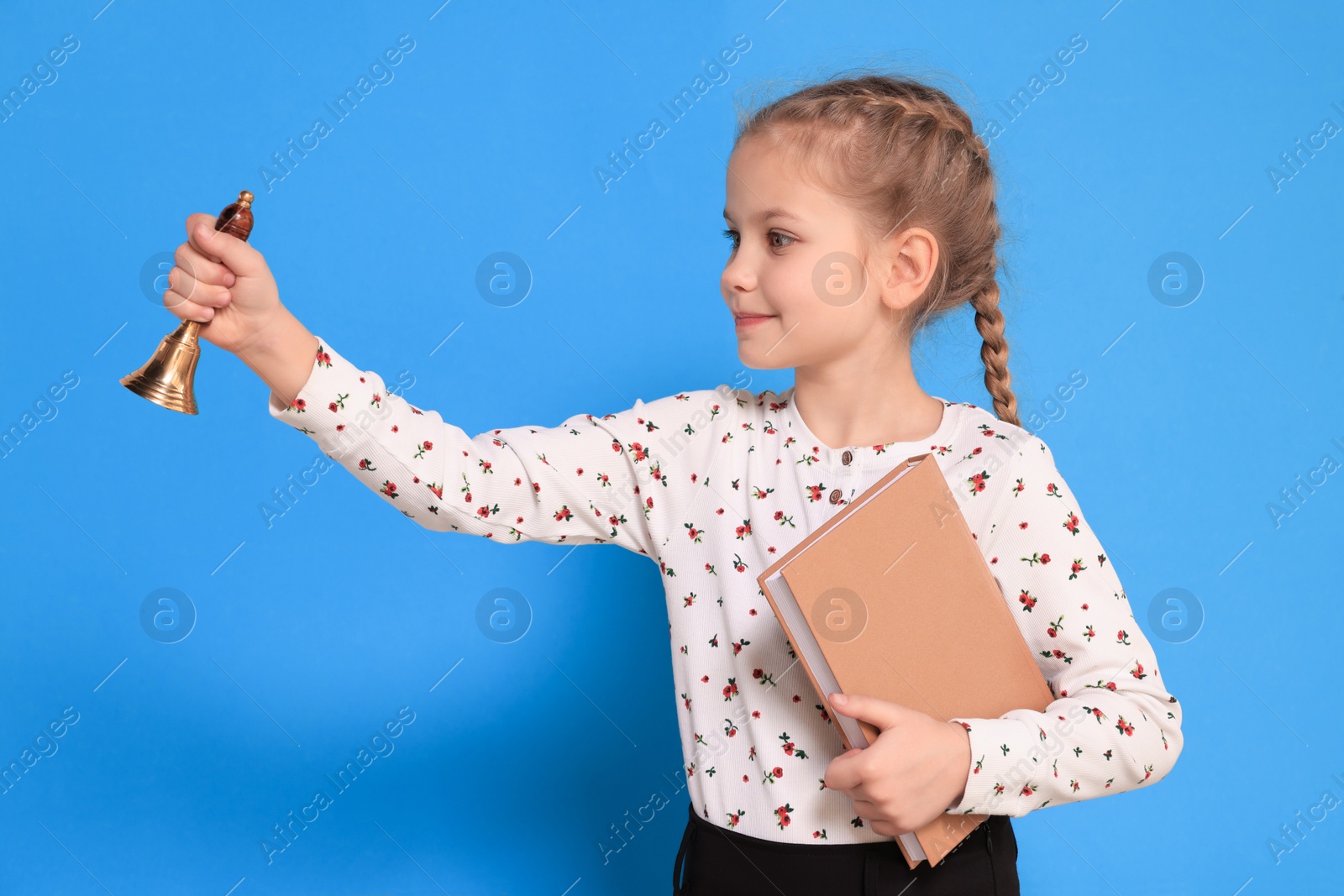 Photo of Pupil with school bell and book on light blue background