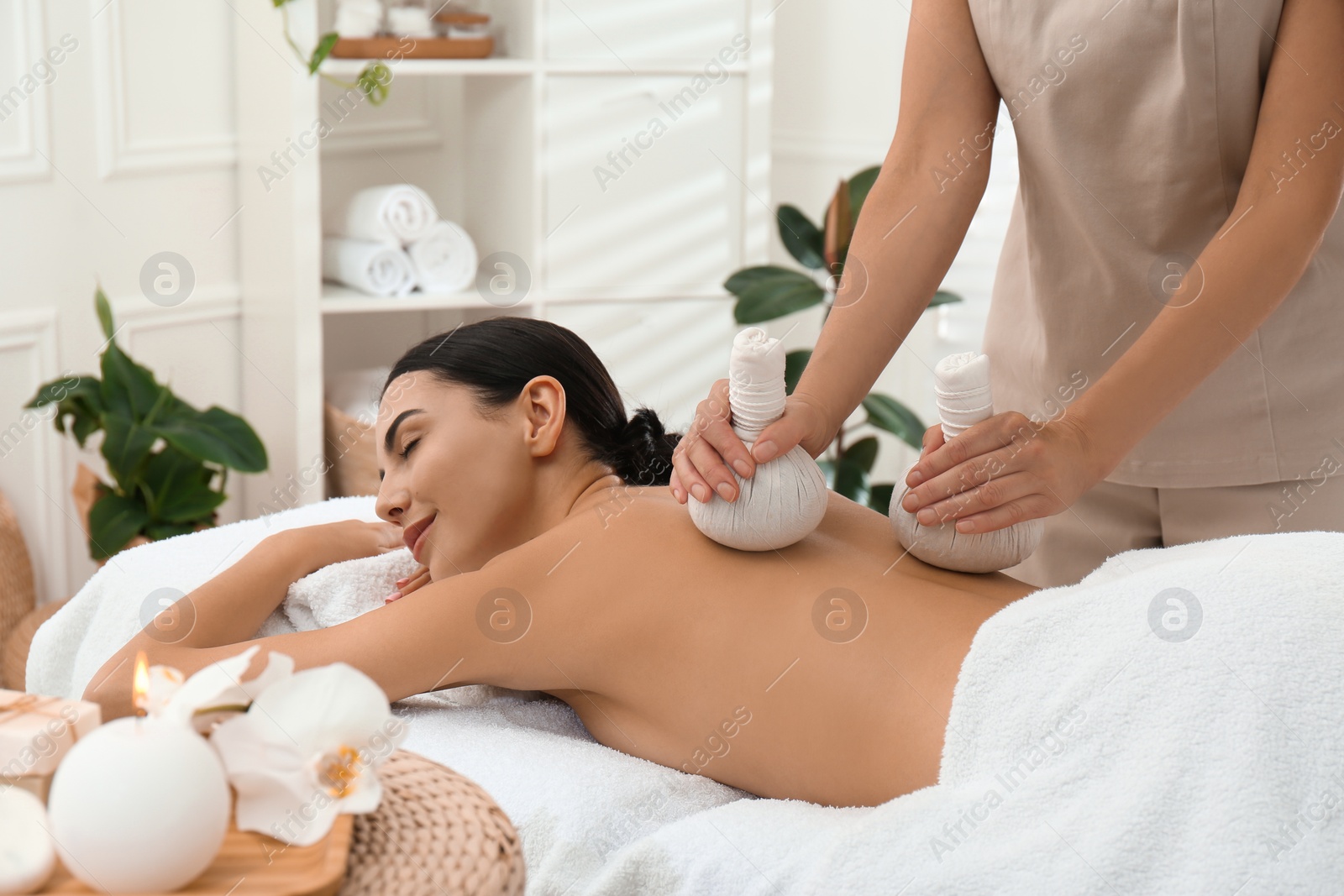 Photo of Young woman receiving herbal bag massage in spa salon