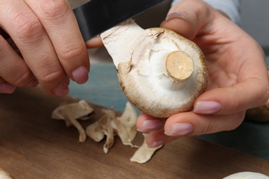 Young woman peeling fresh champignon mushrooms at table, closeup view