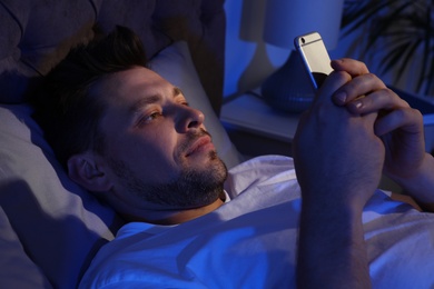 Photo of Handsome man using smartphone in dark room at night. Bedtime