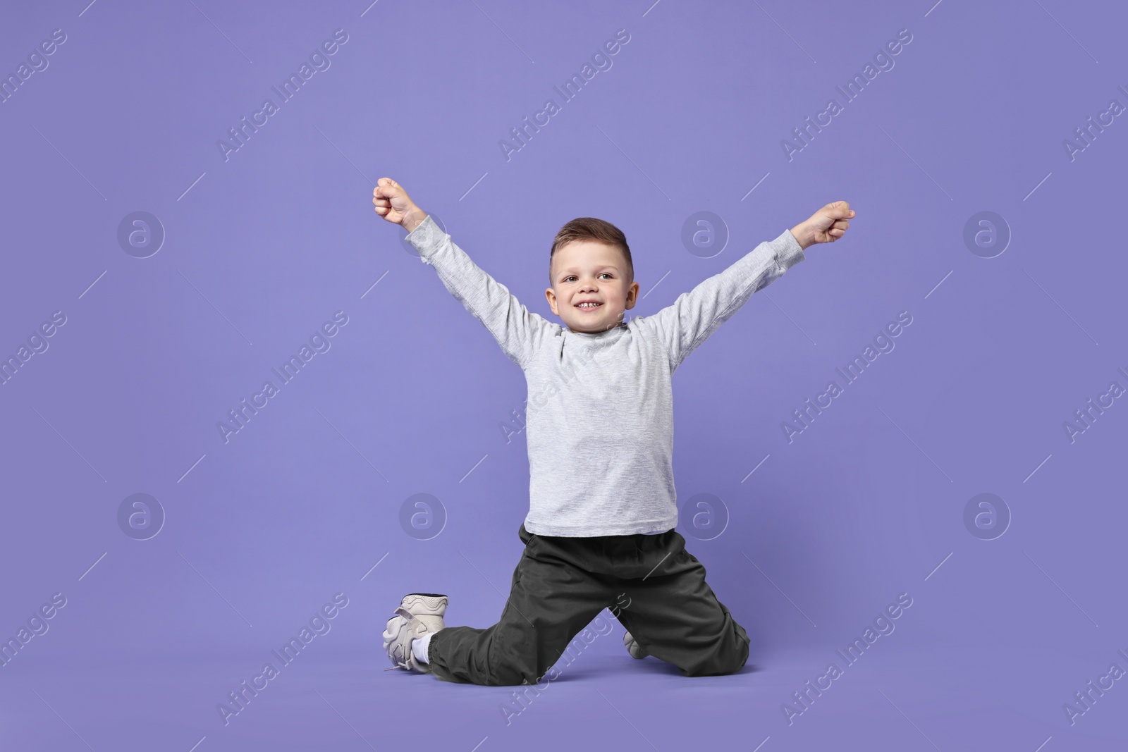 Photo of Happy little boy dancing on violet background