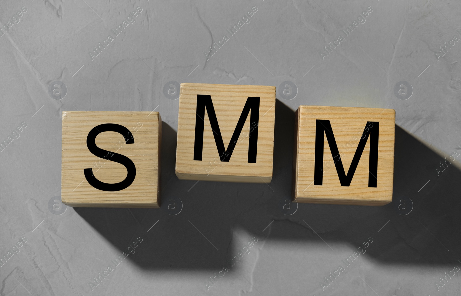 Photo of Wooden cubes with letters SMM on grey stone background, flat lay