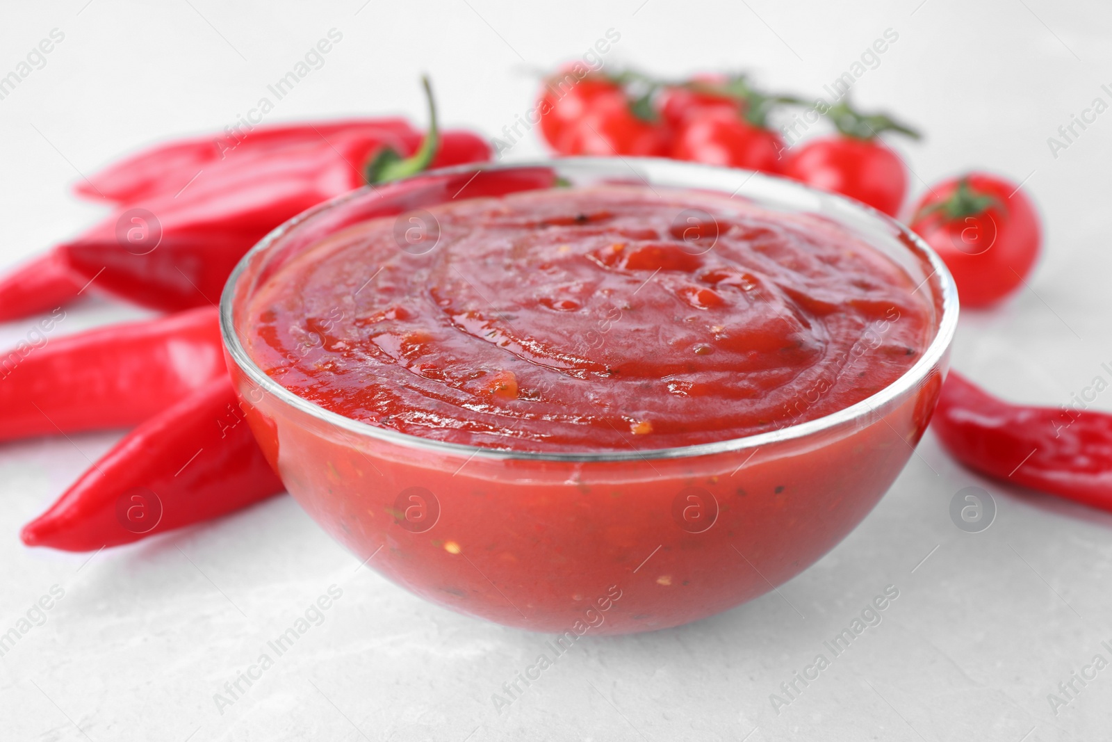 Photo of Bowl of hot chili sauce and vegetables on table, closeup
