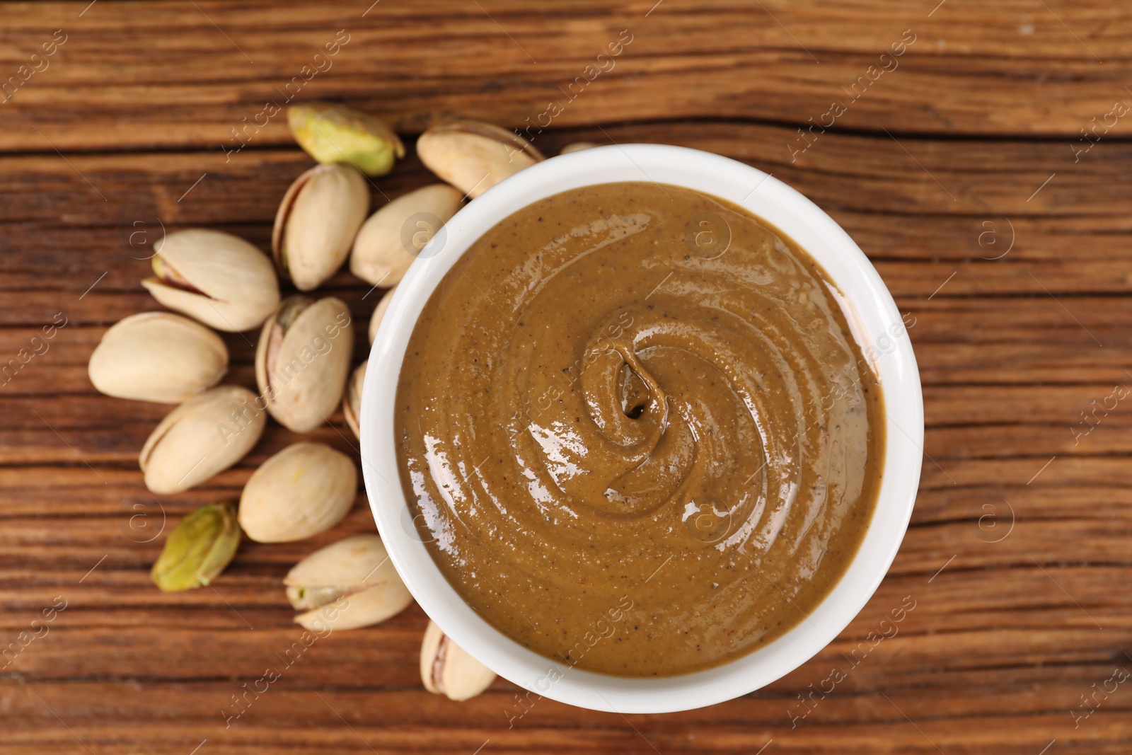 Photo of Delicious nut butter in bowl and pistachios on wooden table, top view